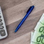 Billetes en euros y calculadora de una persona que está revisando información sobre el impuesto de grandes fortunas